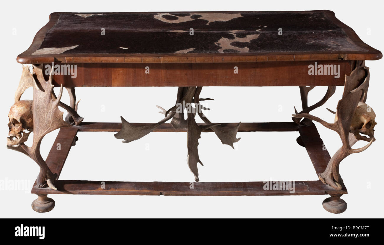 A Bohemian hunting-themed table, from the possessions of the Princes of Schwarzenberg, circa 1870 Walnut veneer on softwood. Plain footrests on compressed ball feet. The legs made of stag antlers, mounted in the middle of each a human skull. The desk top with curved edges and partially covered with dark bull hide (partly heavily worn). On the inside of the frame a brand mark showing the crest of the Princes of Schwarzenberg. Clear traces of wear, the veneer on the footrests partly worn away, small parts missing. Dimensions 157 x 78 x 91 cm. Unusual table, the d, Stock Photo