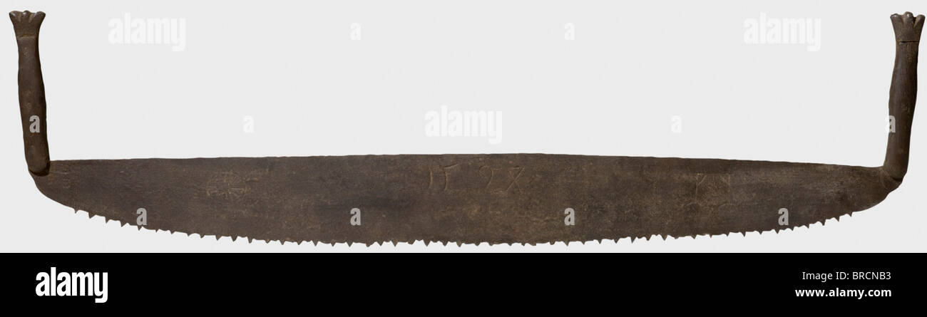 A German executioner's saw, dated 1594 Coarsely serrated saw blade, the front engraved with a wheel and gallows, riveted wood grips on both sides, the handles with forged crown endings. Metal surfaces scarred and rusty, with signs of age. Length 120 cm. In the Middle Ages and the Early Modern Period, the saw torture was a punishment applied especially to agitators and traitors. The delinquent was hung in an inverted position, before the saw was placed at the groin. Contemporary reports describe how the unfortunate victim sometimes remained fully conscious until, Stock Photo