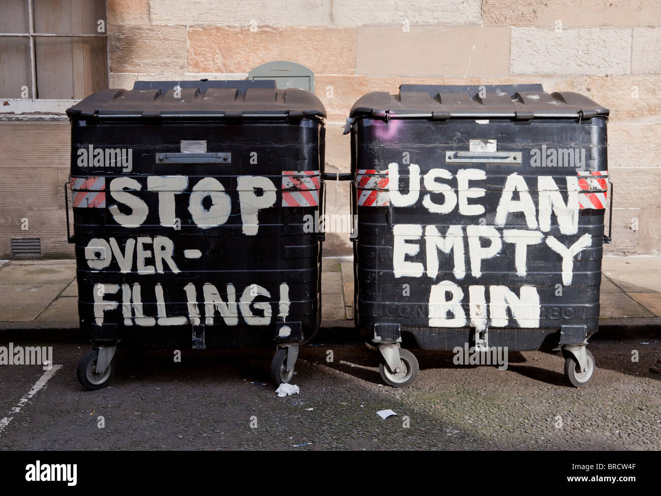 Black Edinburgh city wheely rubbish bins with residents' painted pleas to prevent over-filling Stock Photo