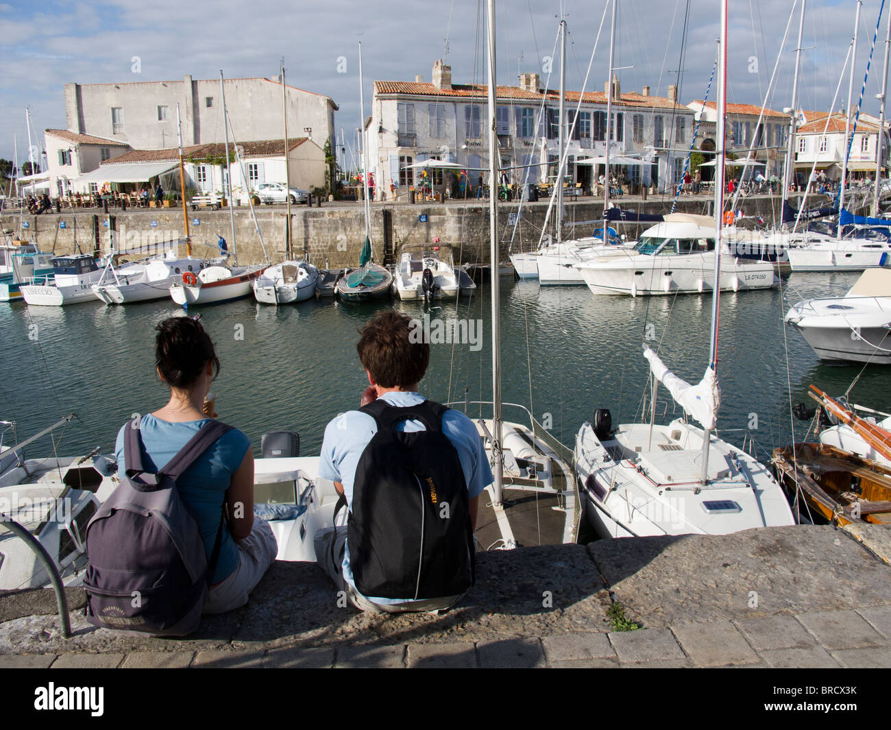 Backpackers sitting on the harbour of the port at St Martin de Re on the Ile de Re, France Stock Photo