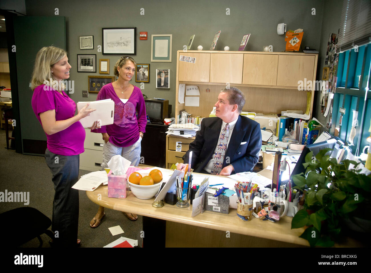 A Southern California school principal meets with two teachers in his office. Note pregnant woman at left. Stock Photo