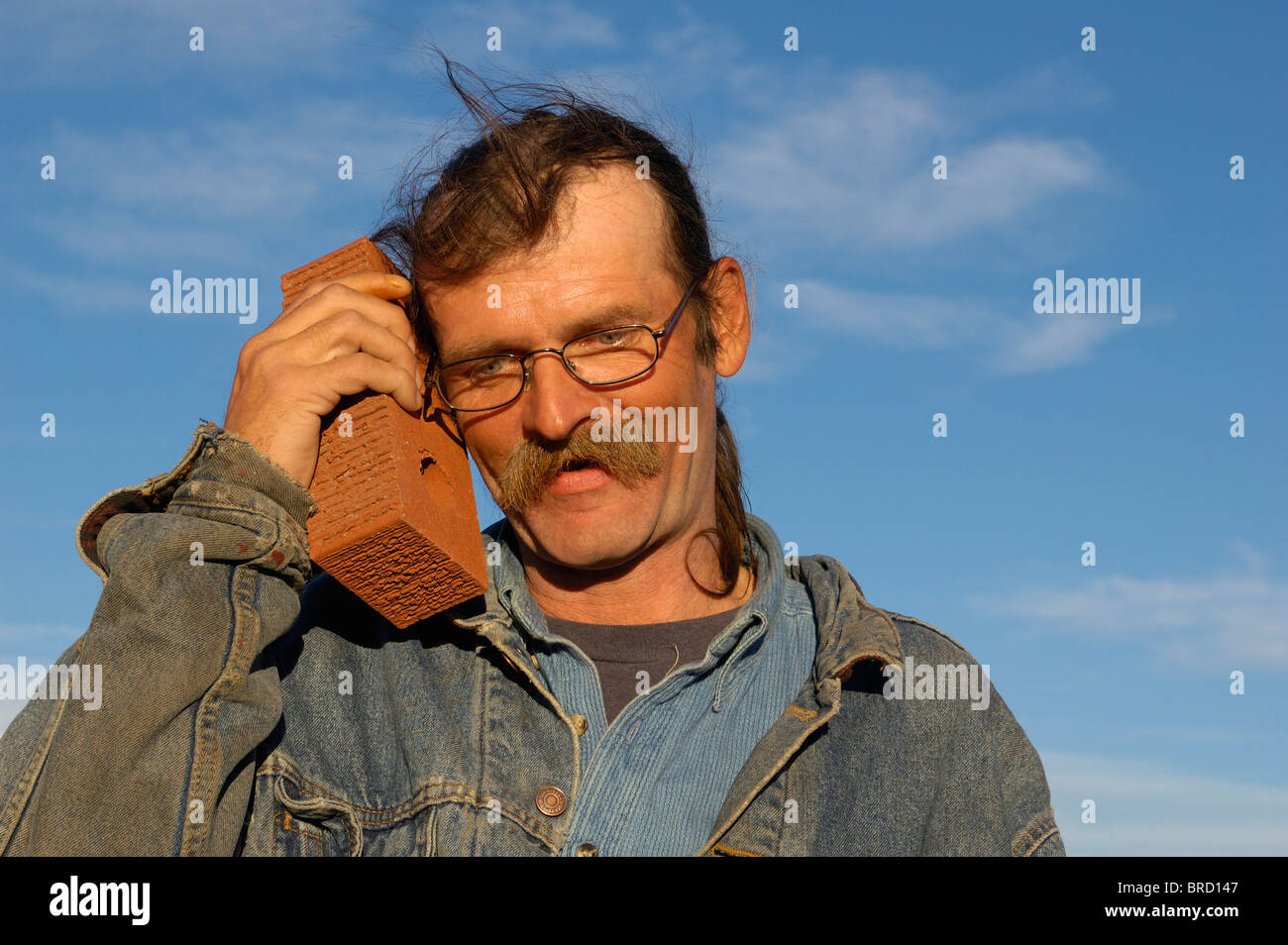 A scruffy man talks to a brick as though it were a mobile phone. Stock Photo
