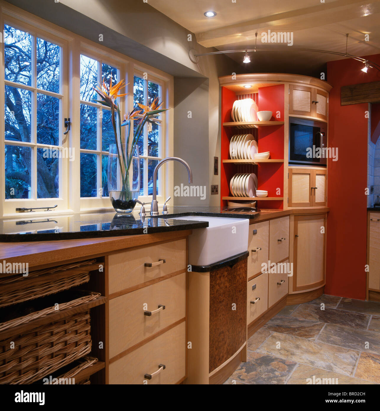 Belfast sink below window in welllit modern kitchen with pale wood