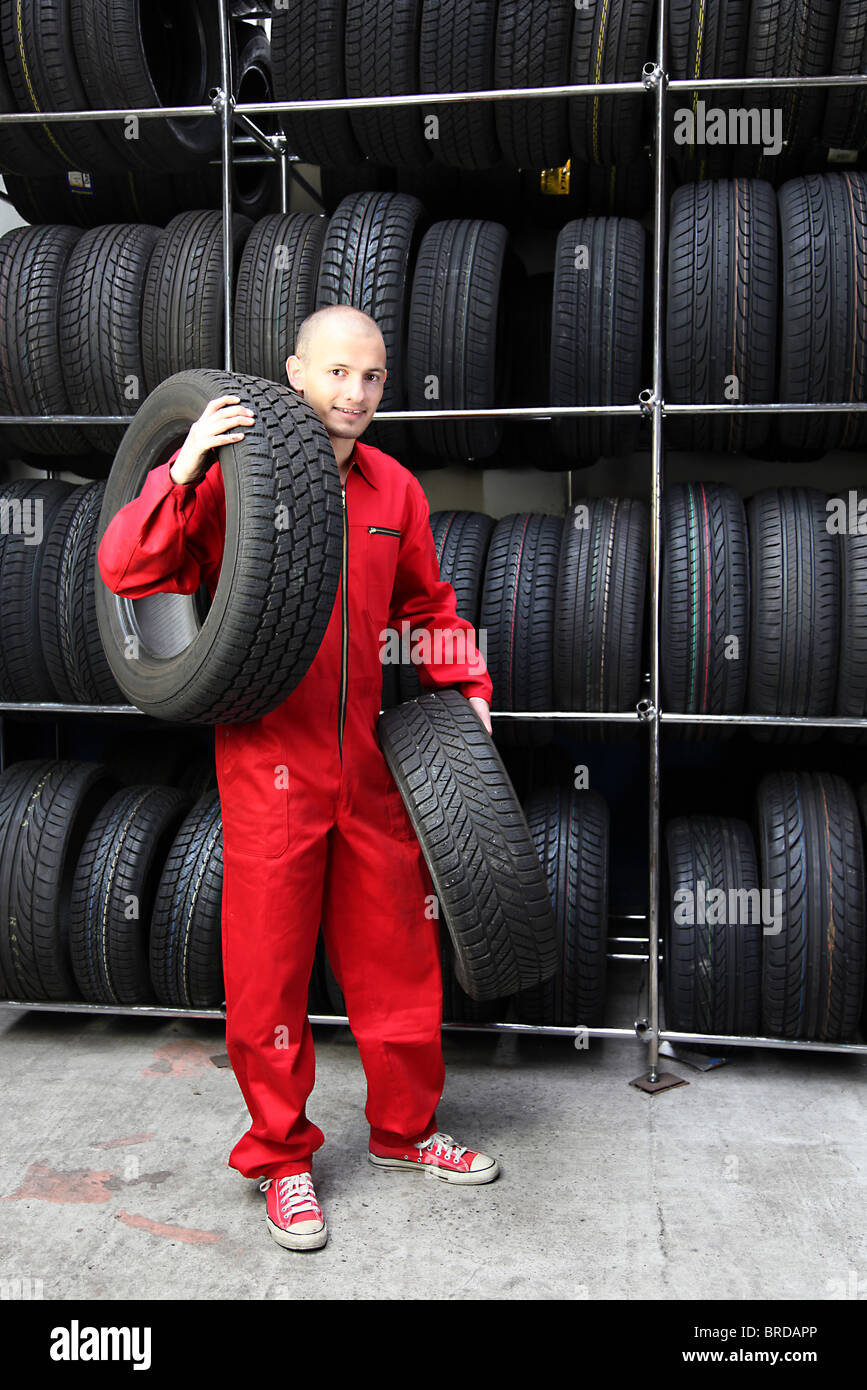 A motivated worker in a tire carrying two tires Stock Photo