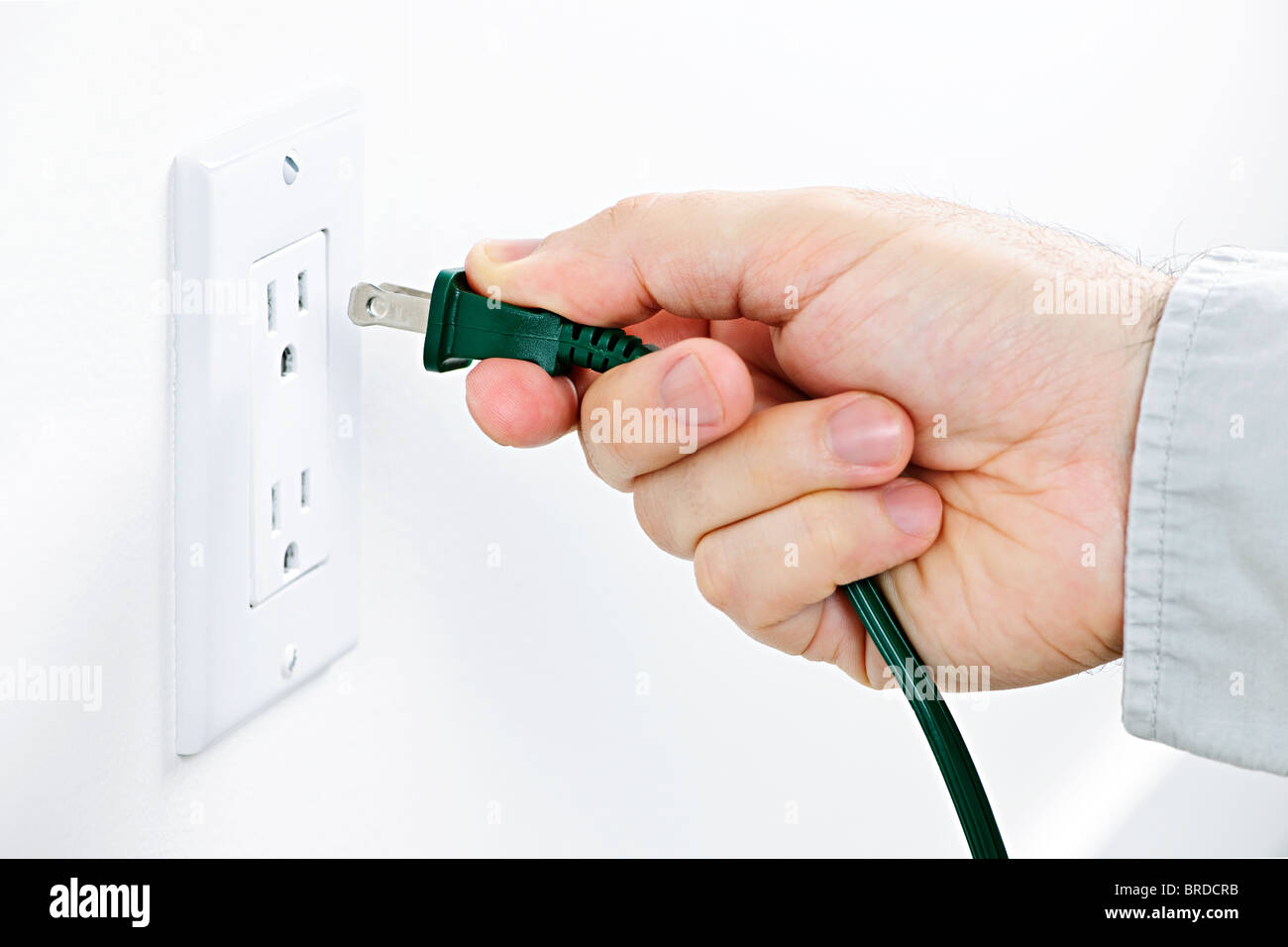 Hand inserting green electrical plug into outlet Stock Photo