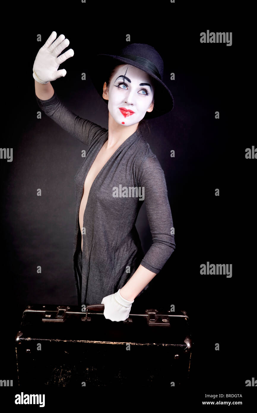 Female mime in white gloves with a suitcase, waving goodbye on a black