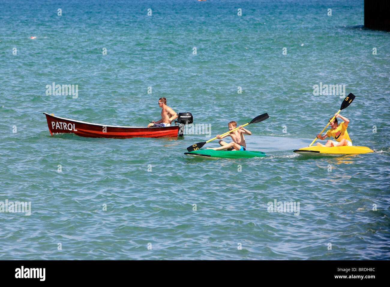 Patrol boat giving advice to two teenage boys on paddle boards at