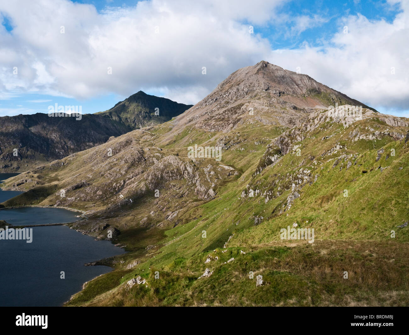 The shapely cone of Crib Goch rises above the lake of Llyn Llydaw, with Yr Wyddfa, the summit of Snowdon, in view behind. Stock Photo