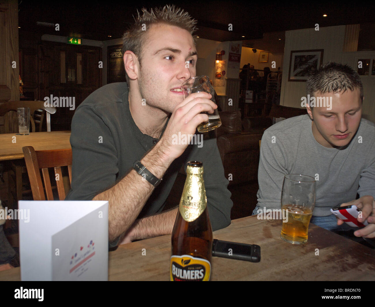 A young man in a pub drinking socially a half pint of lager with