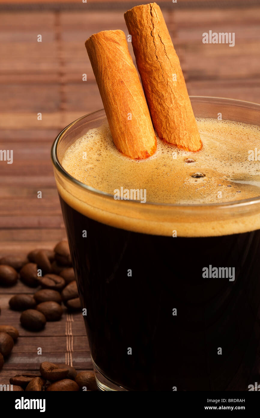 cinnamon sticks inside espresso in a short glass coffee beans aside on