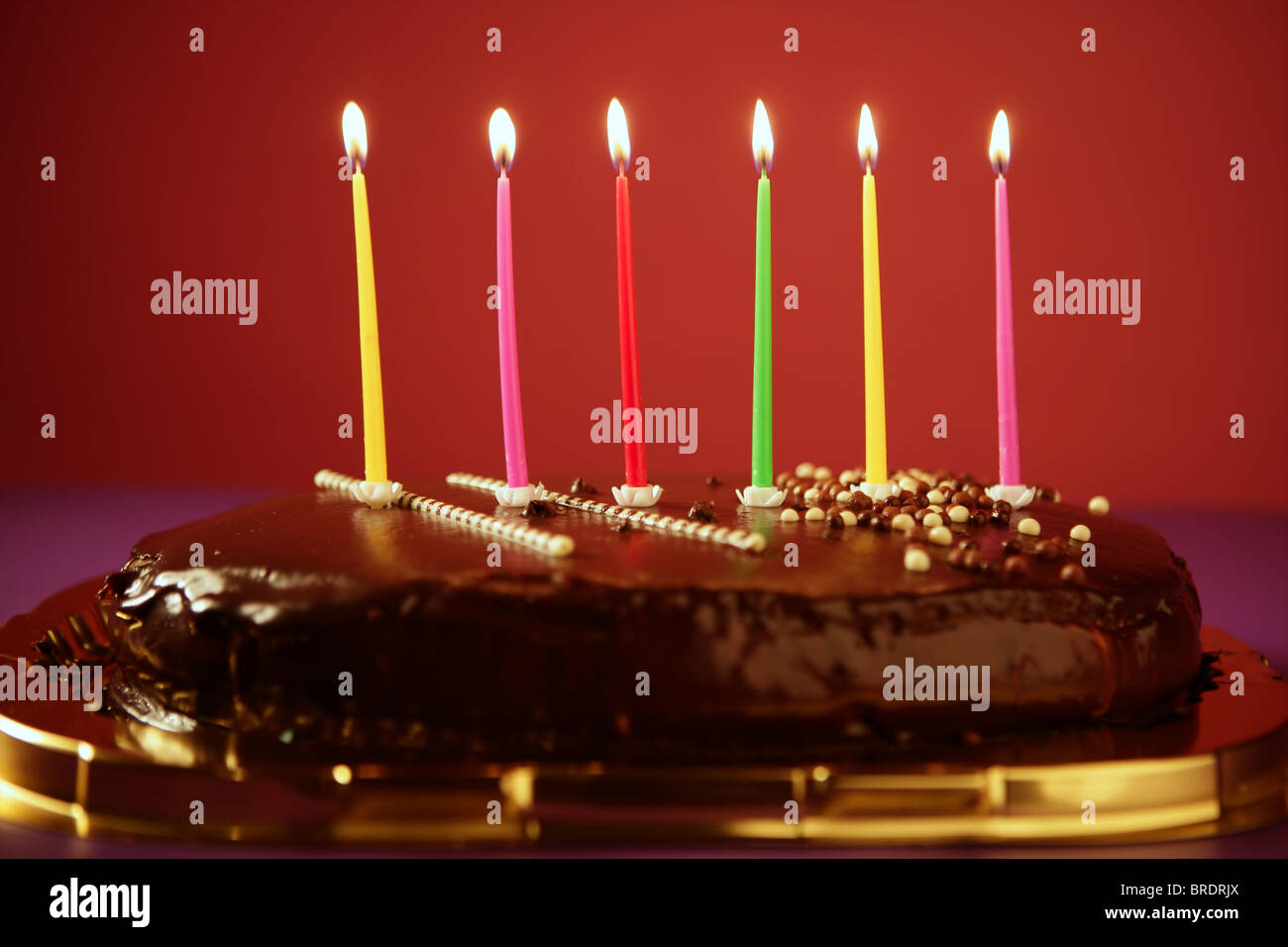 Colorful birthday light candles in a chocolate cake red background ...