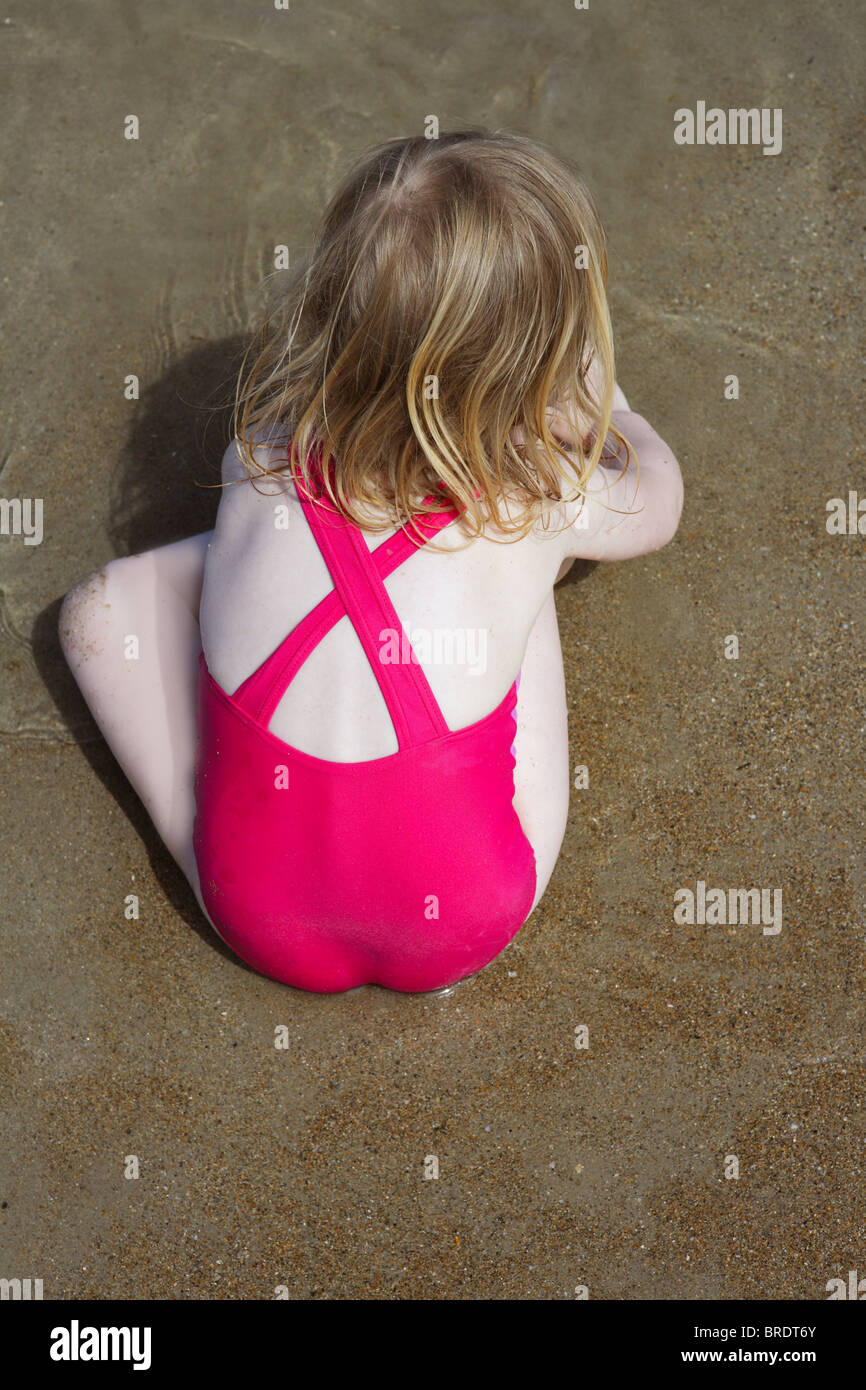 blond little girl swimsuit back high view playing on beach sand Stock
