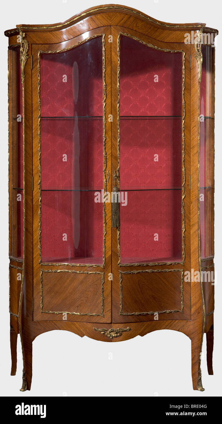A serpentine display cabinet from the parlour décor, ascribed to the Gambs Workshop, Saint Petersburg, 1846. Tropical wood veneer, glass, gilt bronze fittings and red brocade with raised flower decoration. The swing doors and side surfaces with glass inserts, two glass shelves and one brocade-covered wood shelf. One foot with inventory tag 'ON' of Grand Duchess Olga Nikolaevna, attached on the inside the label 'H.V.v.W. G.v.R.' of Duchess Vera of Württemberg, Grand Duchess of Russia. Vintage restoration of the back section. 173.5 x 99 x 40 cm. Provenance: Grand, Stock Photo