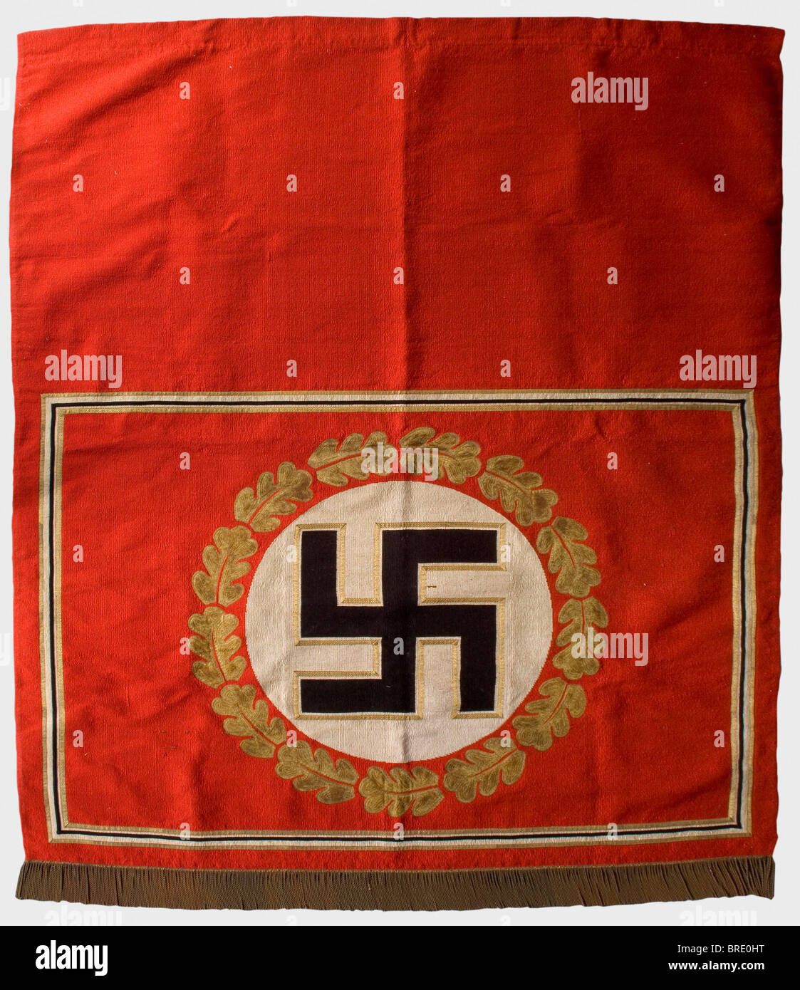 Adolf Hitler - a tapestry, from the Brown House in Munich Heavy version made of red fabric, in the centre a gold-bordered, upright black swastika in a white disc surrounded by gold oak leaf embroidery. Rectangular, black-white-golden border. Fringe trim on the lower edge. The upper edge with a broad hem, inside a sleeve for the wall hanging rod. Small damages, the red silk backing with repairs. Size 220 x 190 cm. From a series of tapestries from Adolf Hitler's personal meeting room in the party building complex 'Braunes Haus' in Munich, Briennerstr. 45. Cf. Her, Stock Photo