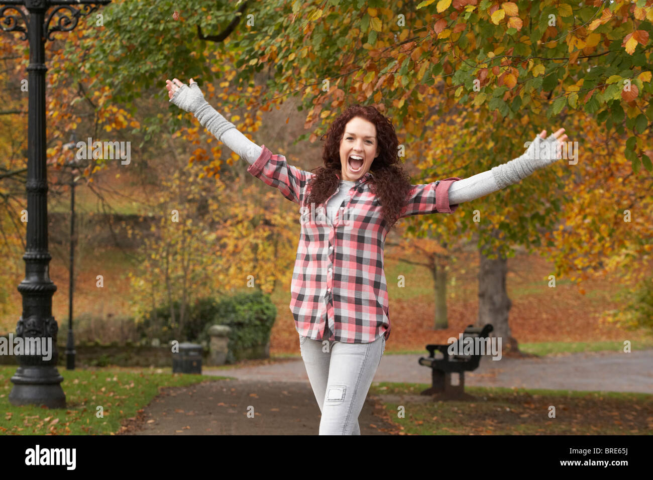 Teenage Girl Standing In Autumn Park With Arms Outstretched Stock Photo
