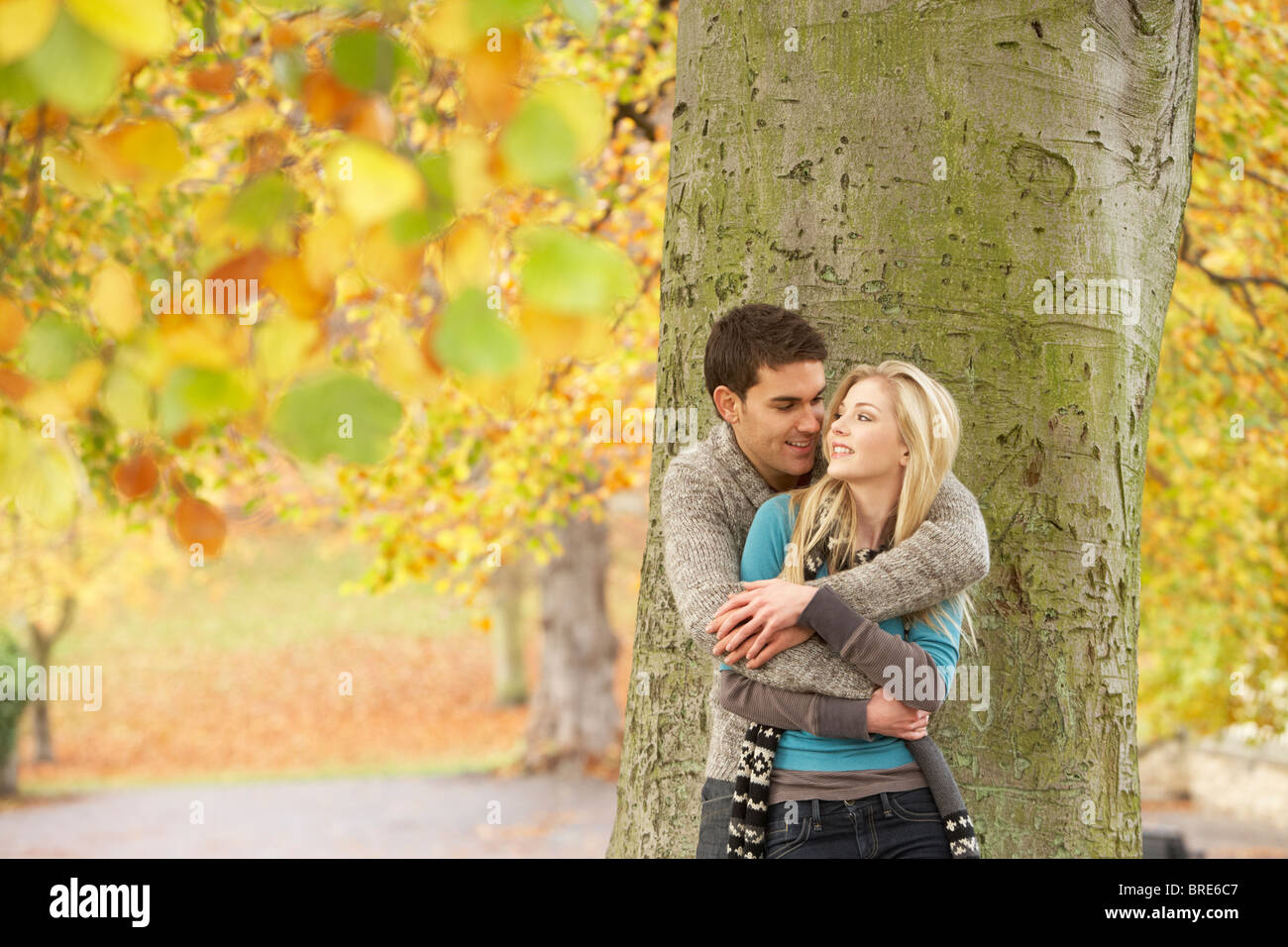 Romantic Teenage Couple By Tree In Autumn Park Stock Photo - Alamy