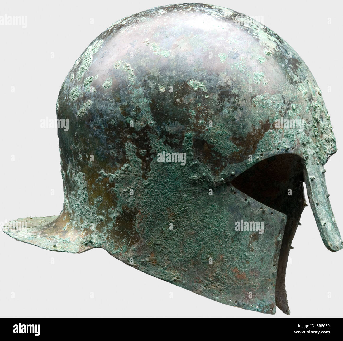 A Corinthian helmet, 7th/6th century B.C. Thick-walled, heavy, bronze Corinthian helmet with a tall skull and extended neck-guard. Large eye cutouts, slightly concave cheekpieces and a sturdy riveted long nose-guard bent outwards. Surrounded with drilled holes, some in pairs, and some still retaining the decorative or lining rivets with round heads. Height 22.1 cm. Weight 1288 g. Metal surfaces with light-brown, dark and light-green patina. Dirt residue inside. Isolated corrosion pits on the surface. Very good metal retention. Axel Guttmann Collection (H 147/ A, Stock Photo