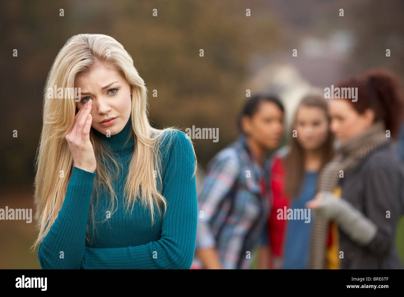 Upset Teenage Girl With Friends Gossiping In Background Stock Photo