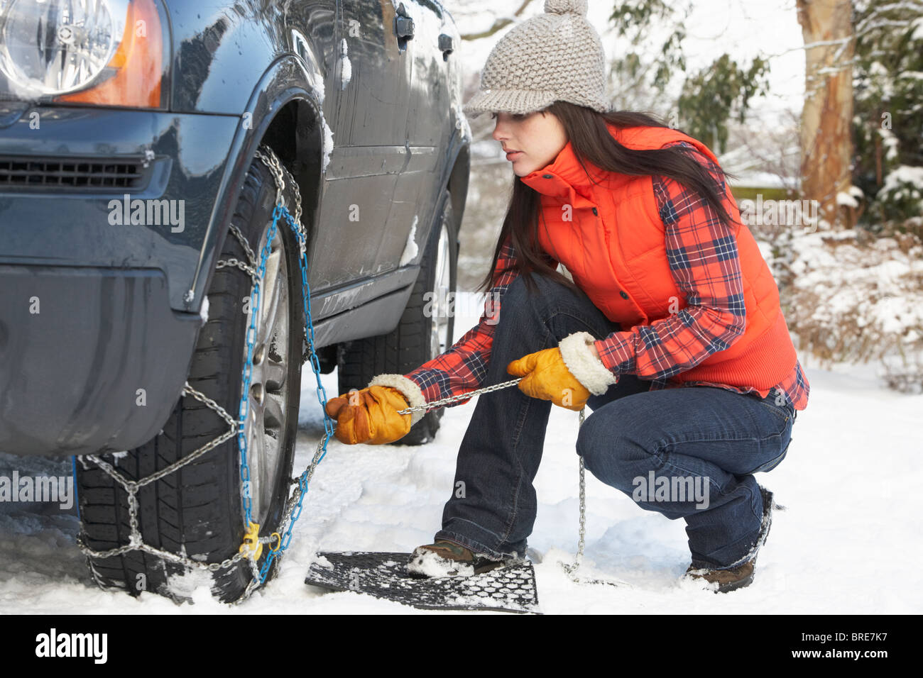 Woman Putting Snow Chains Onto Tyre Of Car Stock Photo
