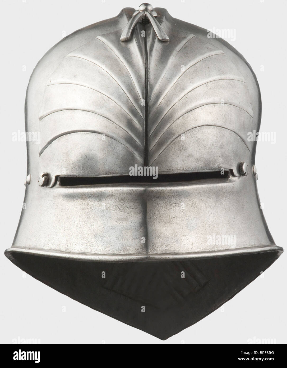 A Southern German late Gothic sallet, Innsbruck(?), circa 1490 The skull forged in one piece with a medial ridge splitting into a double comb over the brow. Three curved flutes on both sides at the back of the head, the pointed tail fluted twice. Surrounding lining rivets. The lower edge turned outward. A reinforcing plate for the brow, made in two pieces, each formed with six ridges. A forked retaining bar screwed on the crown of the skull, and a retaining screw on each side of the eye slit for attachment. On the right side of the nape of the neck a copper sol, Stock Photo