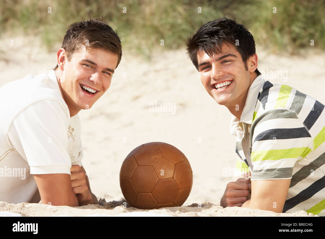 Two Young Men Relaxing On Beach With Football Together Stock Photo