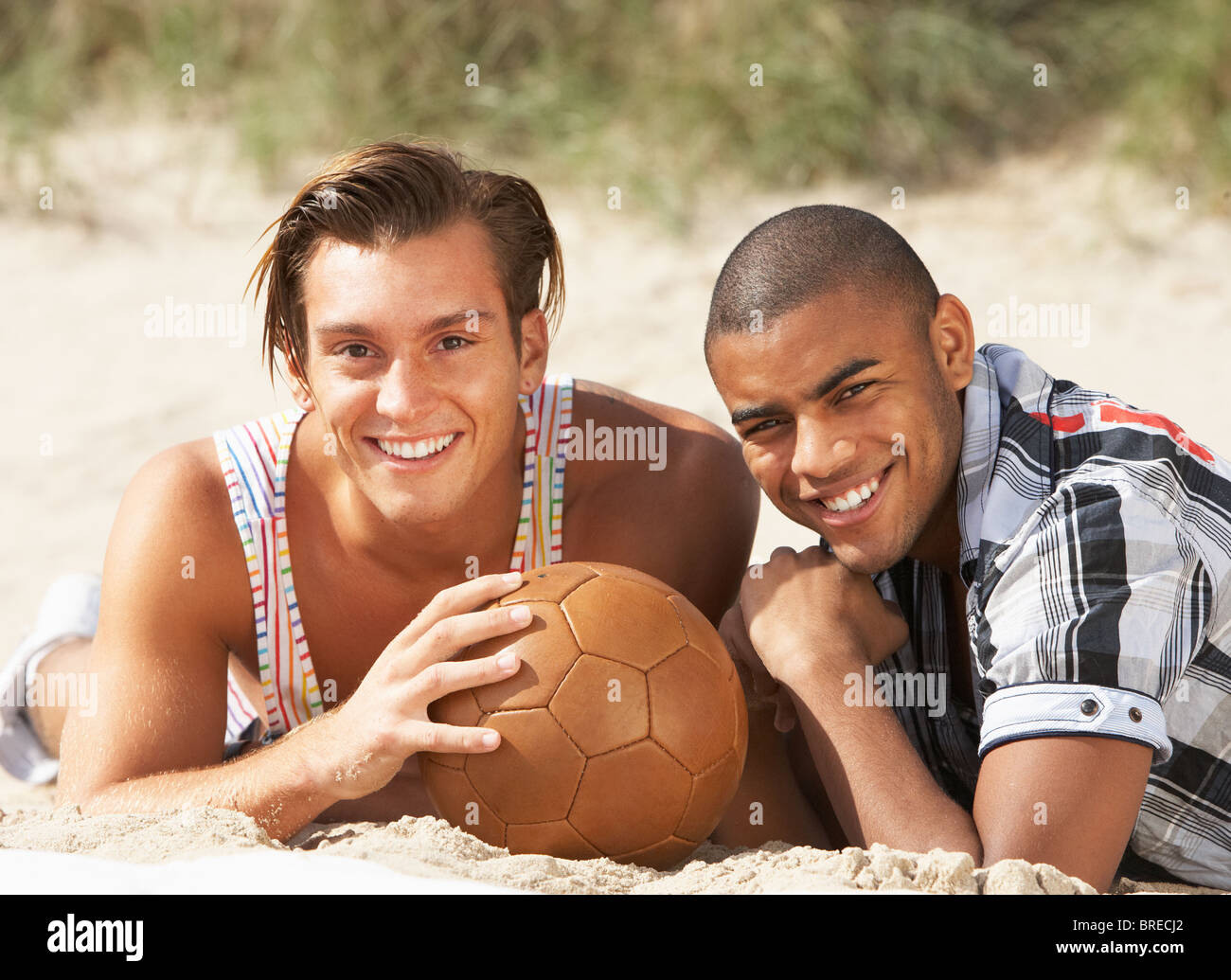 Two Young Men Relaxing On Beach With Football Together Stock Photo
