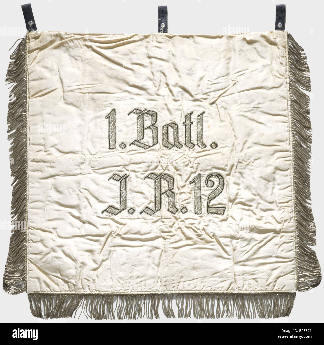 A trumpet banner, of the 1st Battalion/12th Infantry Regiment White silk cloth with an army eagle embroidered in black and brown surrounded by a silver-embroidered oak leaf wreath over an iron cross and four applied swastikas in the corners. Silver fringes on three sides. Three leather loops. On the reverse side the silver-embroidered unit name. Dimensions ca. 53 x 56 cm. Slightly stained, otherwise in very good condition with bright colours. Of great rarity. historic, historical, 1930s, 1930s, 20th century, infantry, military, armed forces, militaria, object, , Stock Photo