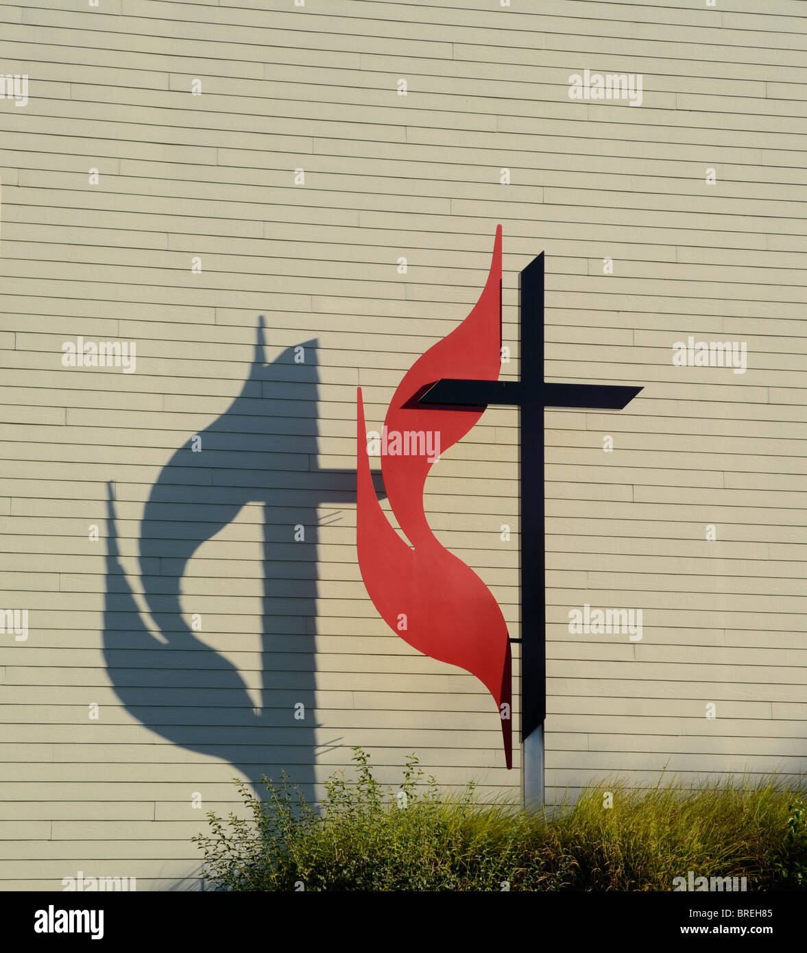 A metal Cross and Flame with shadow, a symbol of the United Methodist Church, outside against a wall of a church building. Stock Photo