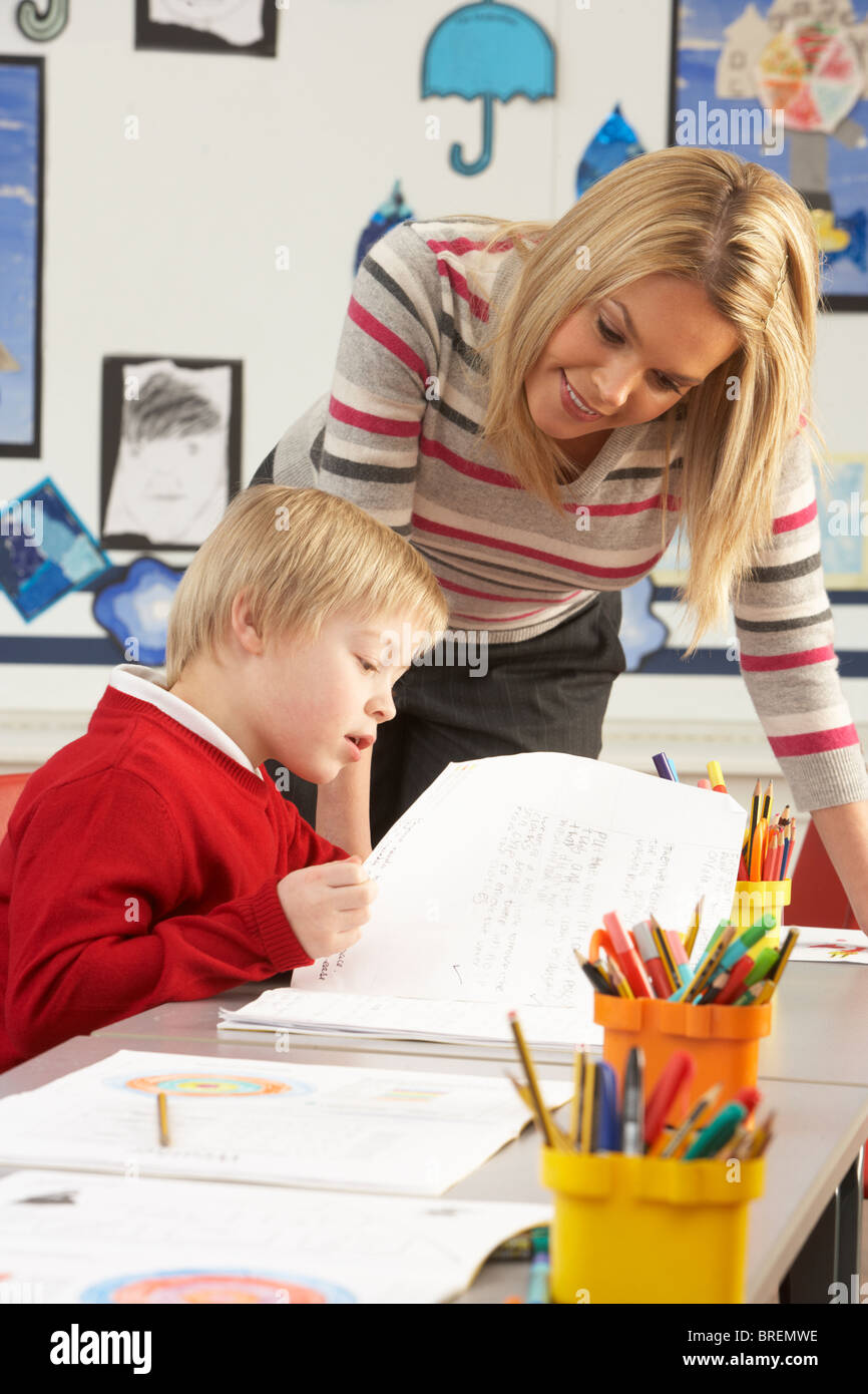 Male Primary School Pupil And Teacher Working At Desk In Classroom Stock Photo