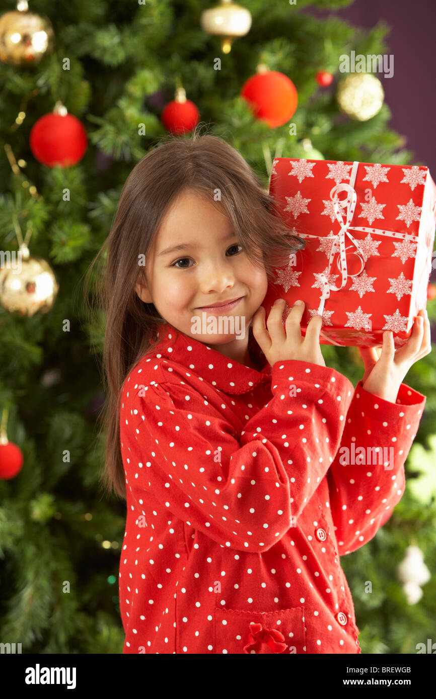Young Girl Holding Wrapped Present In Front Of Christmas Tree Stock ...