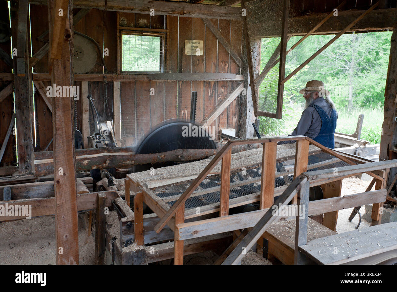 Lumbermill worker squares a log. A lumber mill worker uses a large saw