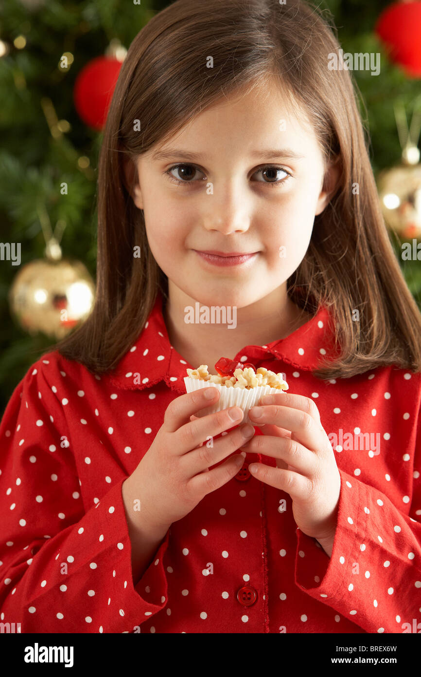 Young Girl Eating Christmas Cake In Front Of Christmas Tree Stock Photo