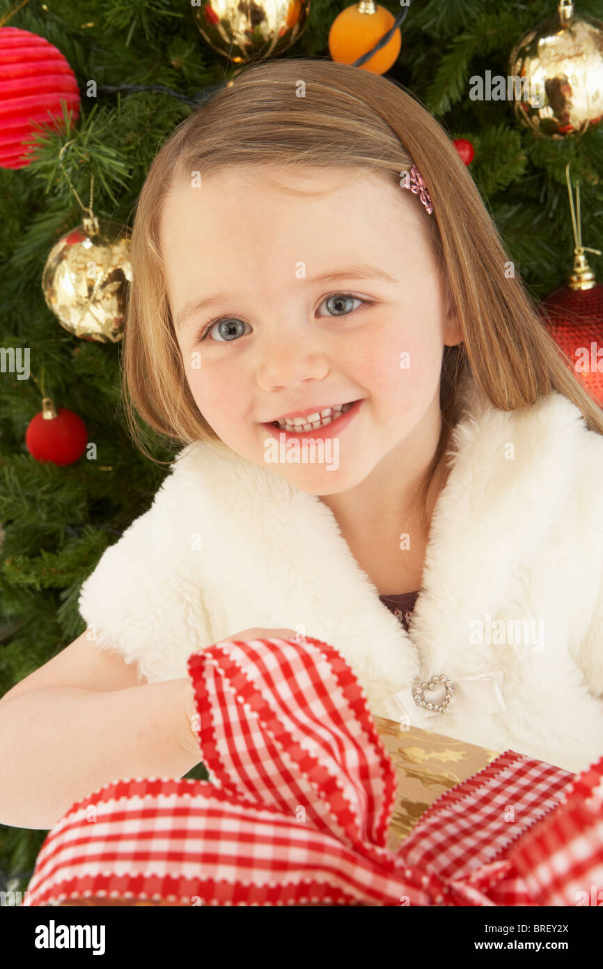 Young Girl Holding Gift In Front Of Christmas Tree Stock Photo - Alamy