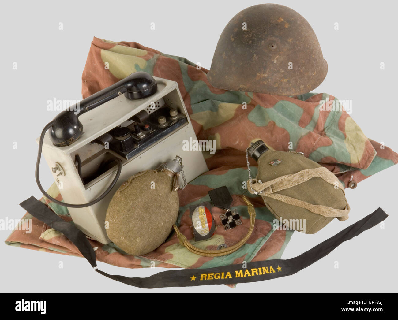 A group of Italian Army items, including a grey-green M33 steel helmet, very corroded paint, interior and chinstrap pretty damaged. Italian field telephone in light grey carrier box with handset. BEVO 'OB' insignia with fasces and national colours. MVSN headgear with golden chinstrap. Two complete Italian canteens with strap and cover. A three-tone Italian camouflaged quarter shelter, 'Regia Marina' navy cap ribbon, patriotic insignia illustrating the Italo/German friendship, an Arditis decoration., historic, historical, 1930s, 20th century, object, objects, st, Stock Photo