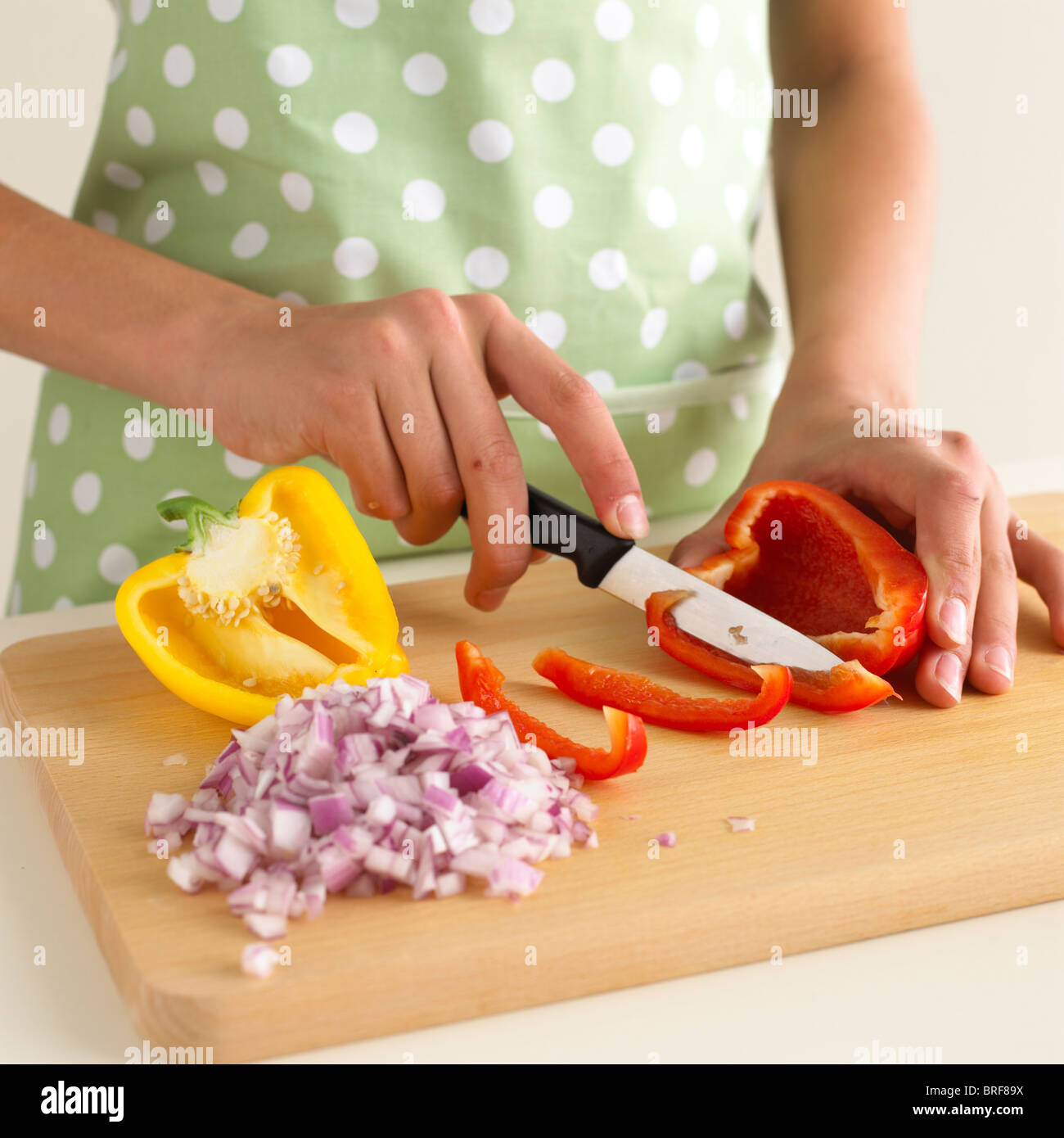 Woman slicing red pepper next to diced red onion and half yellow pepper
