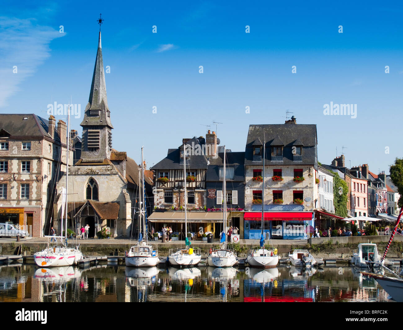 The port in Honfleur, in France, with the town's museum, with spire, and yachts moored at the quayside Stock Photo