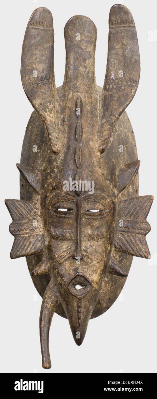 A Kpelie mask of the Senufo people, Ivory Coast, first quarter of the 20th century. Delicately carved wood mask with tri-lobed ornamentation (small break) and characteristic pointed elements attached to the temples and chin (one broken off). Slit-like eyes, oval, strongly protruding mouth, geometrical tribal scars. On the edge circumferential fastening holes for the headdress of natural fibres. Lightly patinated, signs of age and wear. Height 32 cm. The mask comes from the holdings of the Musée d'Art Africain founded by Theodore Monod in Dakar in 1936, which pr, Stock Photo