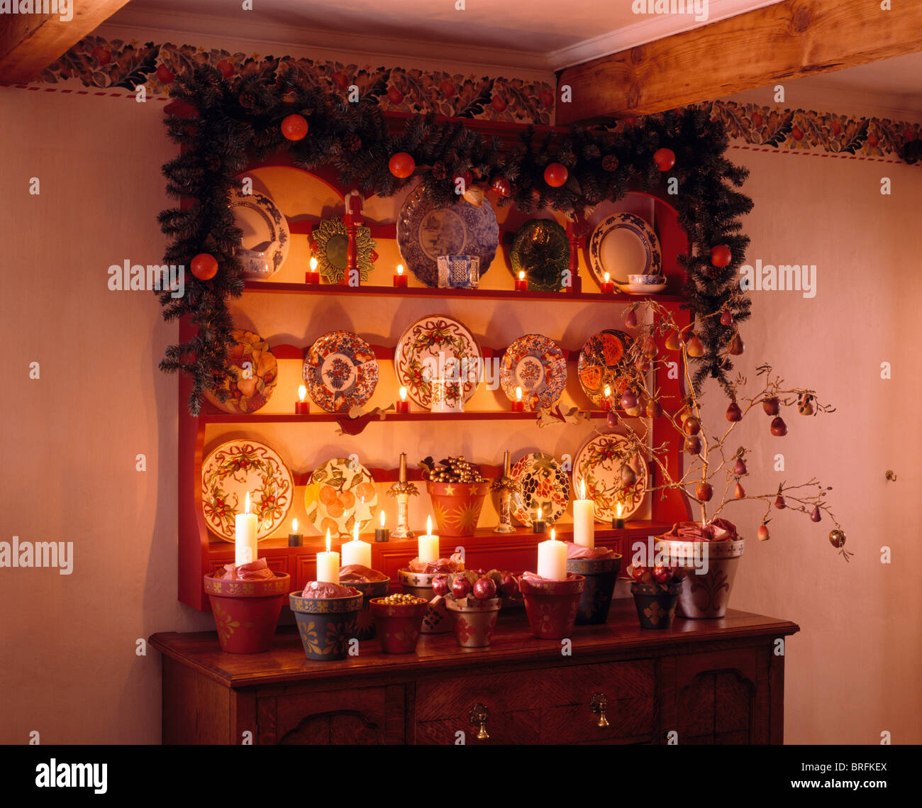 Christmas garland on shelves above sideboard with lighted candles and pottery plates Stock Photo