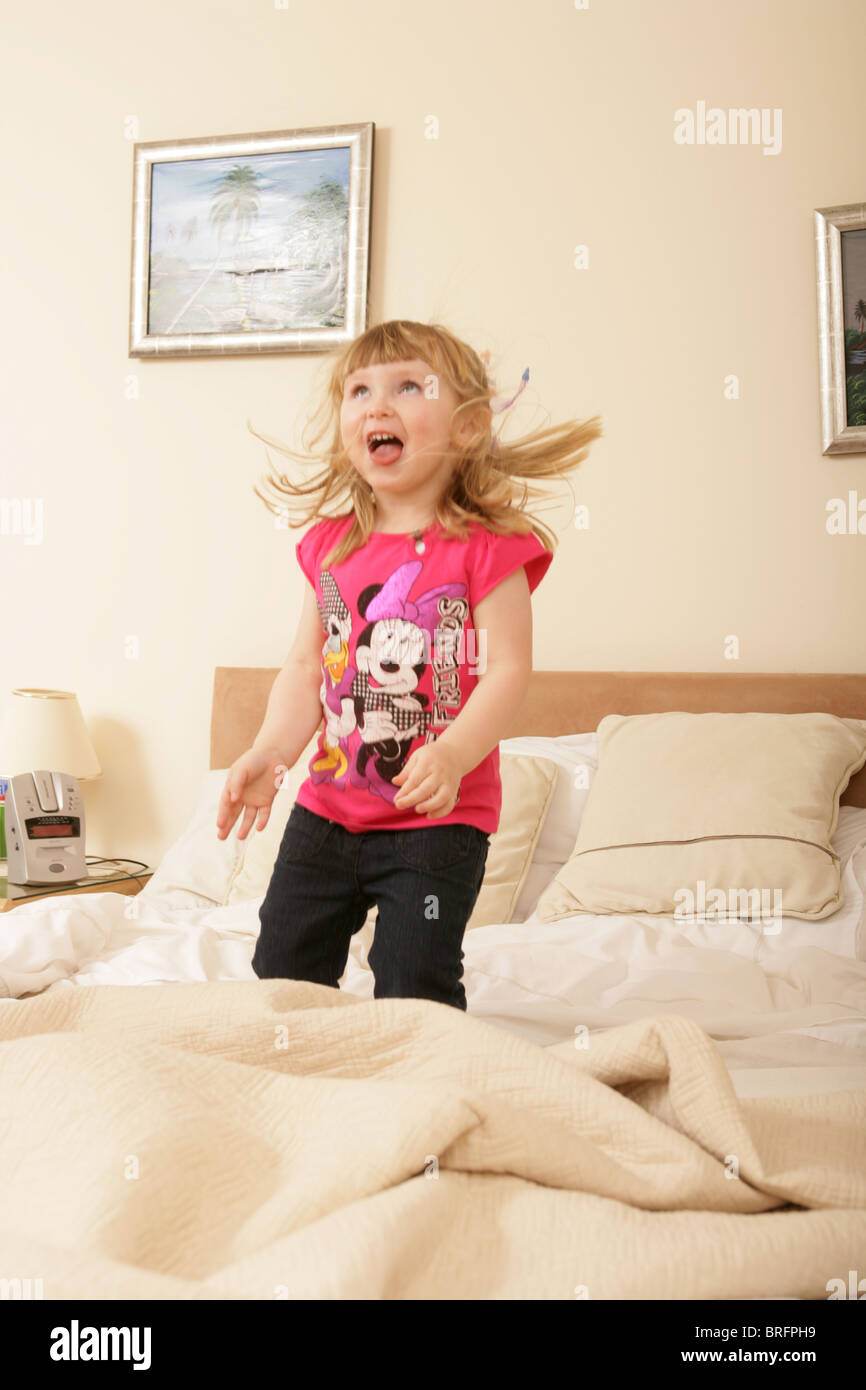 Two year old girl bouncing on her parents bed. Stock Photo