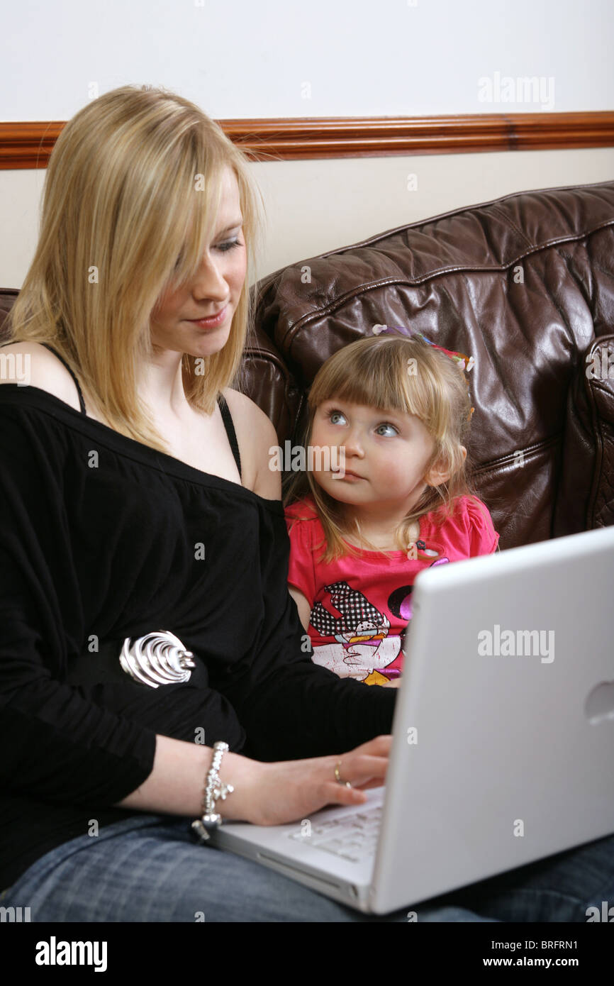 Two sisters sitting on a sofa using a laptop Stock Photo - Alamy