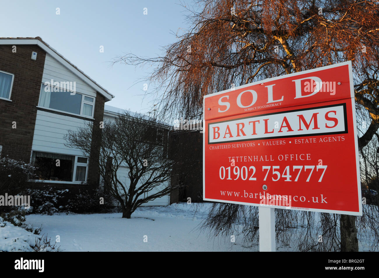Bright red estate agent's sold sign outside a house in the winter with
