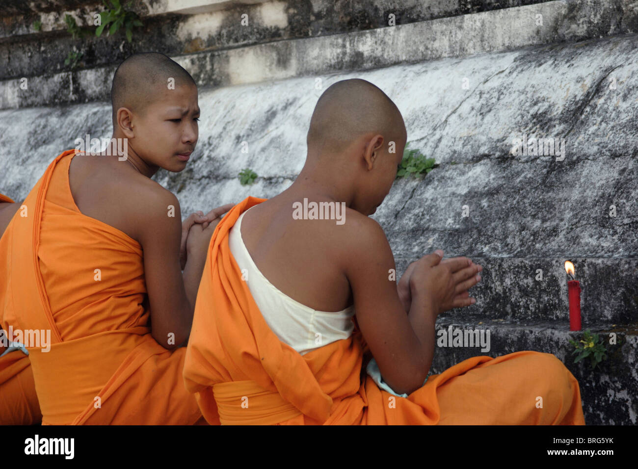 Two novice monks pray at the base of a large stupa at historic Wat Hua Kuang in Nan, Thailand. Stock Photo