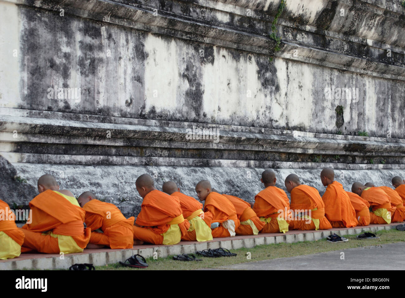 Novice monks pray and study at the base of a large stupa at historic Wat Hua Kuang in Nan, Thailand. Stock Photo