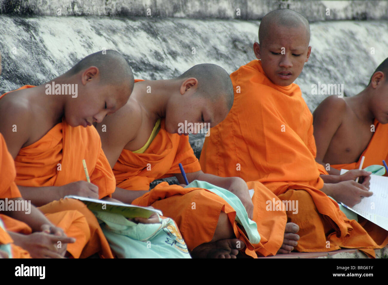 Novice monks study at the base of a large stupa at historic Wat Hua Kuang in Nan, Thailand. Stock Photo
