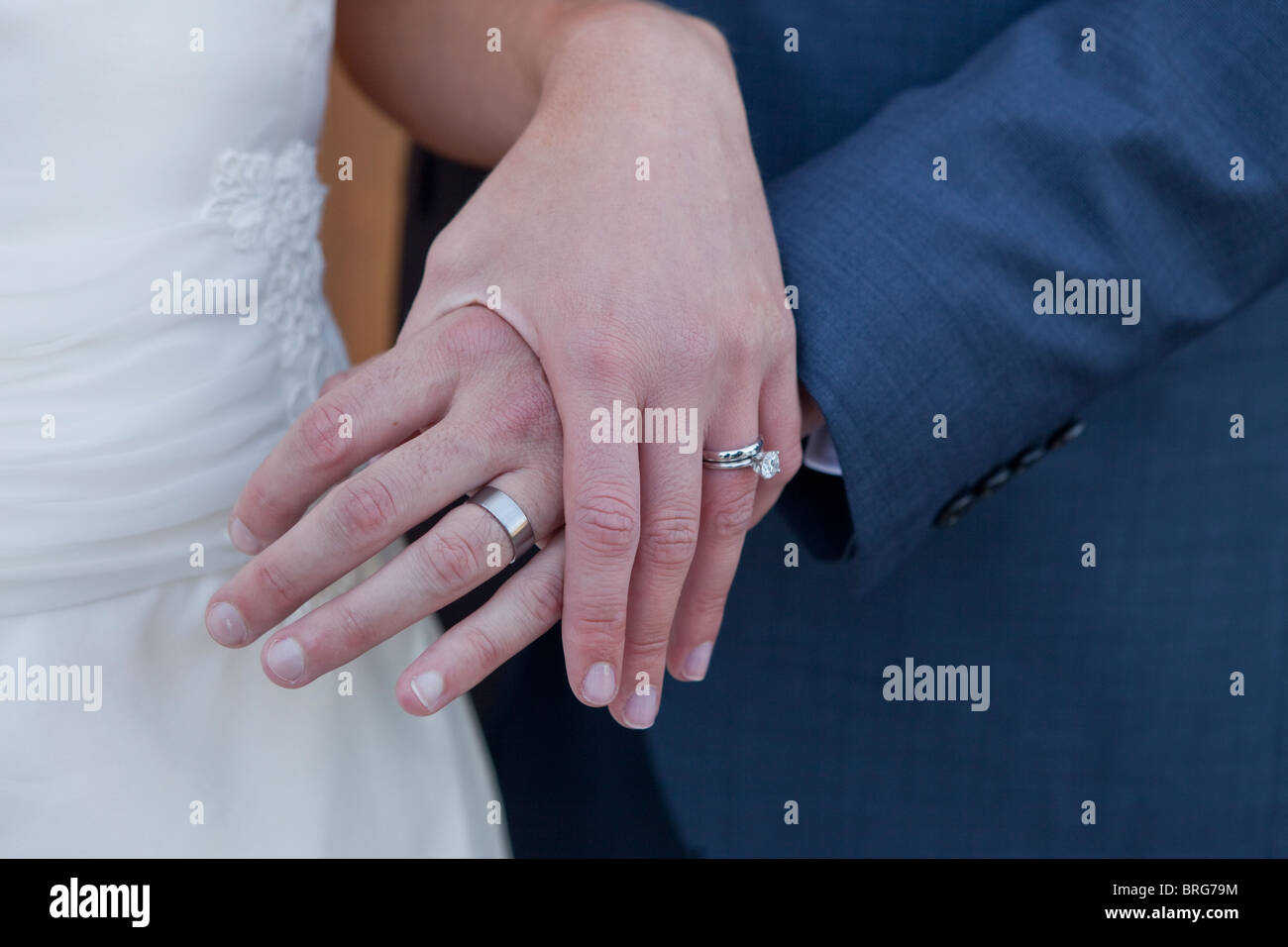 Closeup of newlyweds holding hands with wedding rings visible. Stock Photo