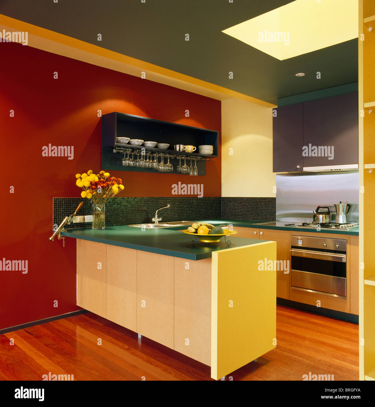 Green worktops on pale yellow and wood fitted units in modern kitchen with red wall Stock Photo