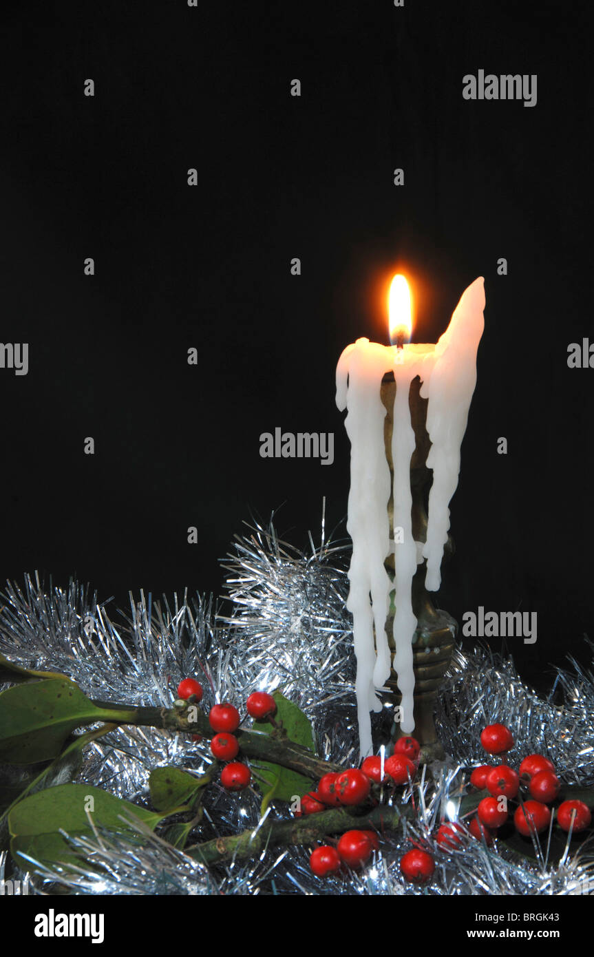 A burning candle, dripping with wax, surrounded by tinsel and holly berries at Christmas. Dorset, UK December 2008 Stock Photo