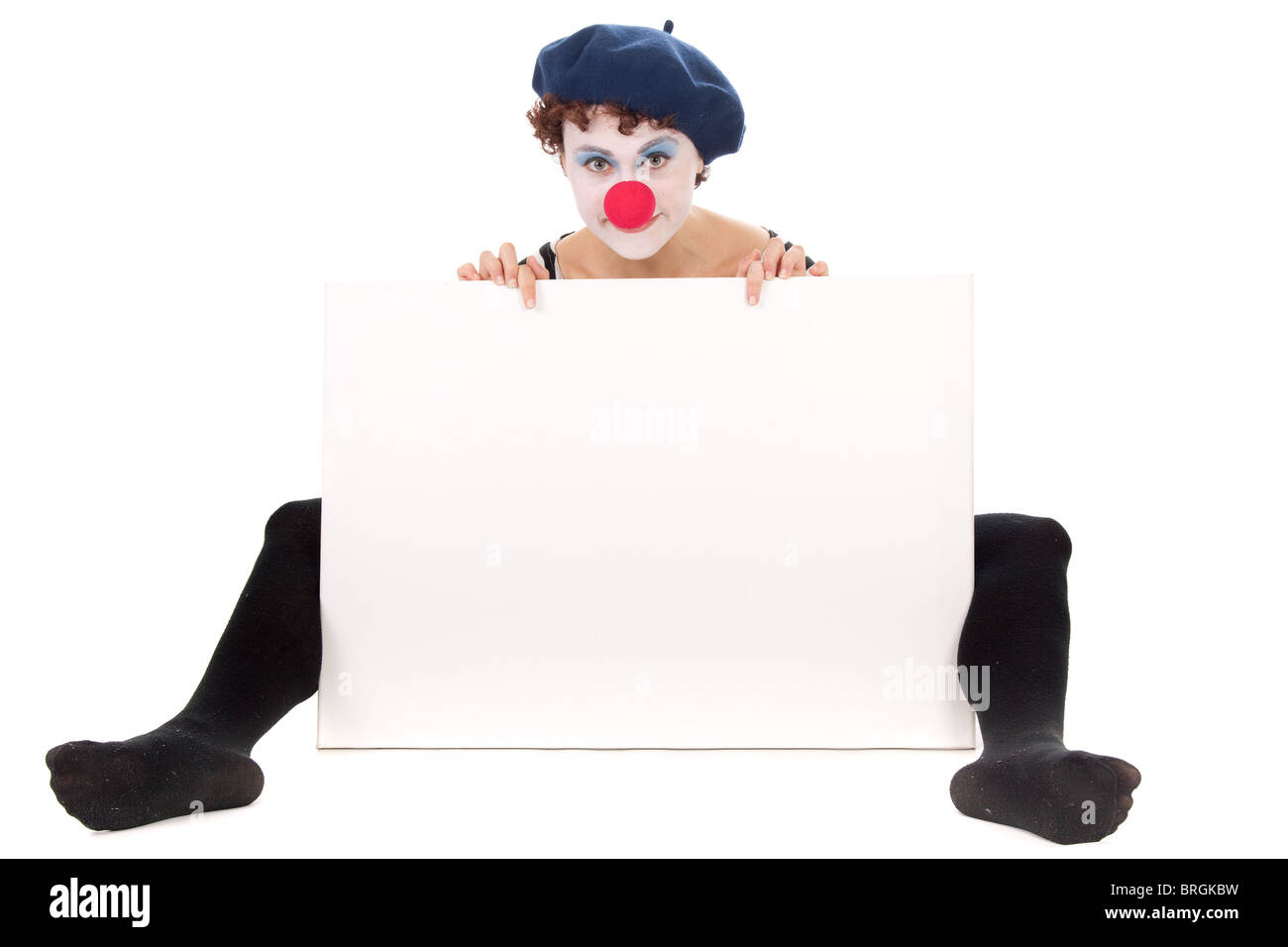 young woman wearing clown face seated on floor and presenting white billboard. Stock Photo