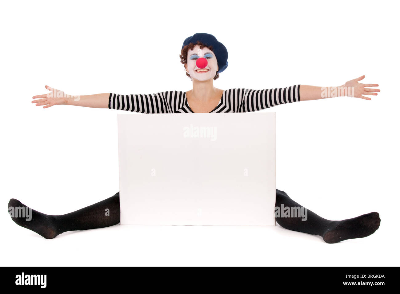 cheerful clown woman seated on floor and presenting white billboard Stock Photo