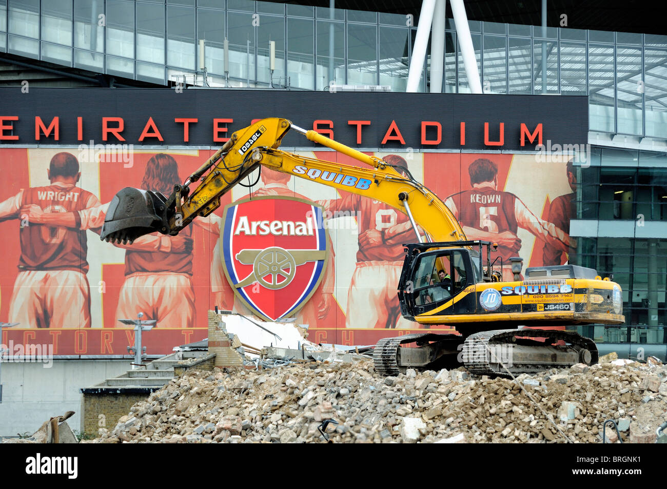 Excavator on pile of rubble in front of the Emirates Stadium, part of the Queensland Road development Holloway London UK Stock Photo
